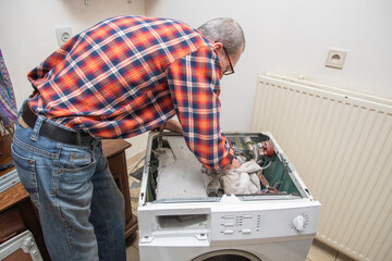 gray-haired man The owner is a jack of all trades who can check a broken washing machine himself, detect the breakdown and repair it, high quality photo