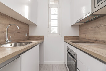 Newly renovated small kitchen with white wooden cabinets, wooden countertop with backsplash,...