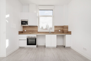 Fototapeta na wymiar Front of a recently renovated kitchen with white wooden furniture, wooden countertop