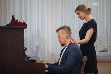 A musician plays the piano while his woman walks by.