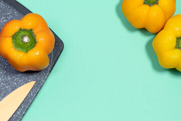 Food background. A yellow bell pepper on a cutting board next to a knife on an aquamarine...