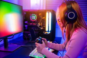 Gamer using joystick controller for virtual tournament plays online video game with computer neon lights, woman wear gaming headphones playing live stream esports games console at home - obrazy, fototapety, plakaty