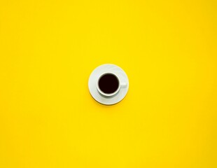 On a bright yellow background, a white cup with black coffee stands in the center.  Space for copy text, flat lay.  Fragrant, delicious hot coffee.