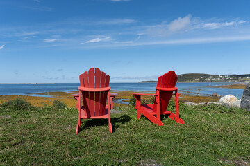 Red chairs at Rocky Harbor in Gros Morne National Park, a Canadian national park and World Heritage Site in Newfoundland. Original red chairs placed throughout Canadian National Parks.  - obrazy, fototapety, plakaty