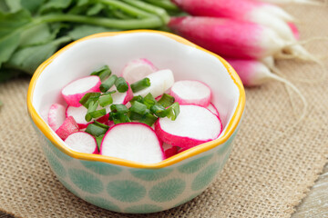 Light salad of raddishes and green onion on the wooden table.