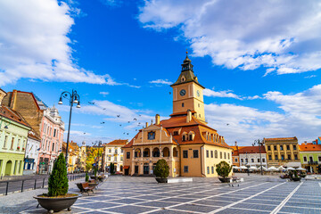 Fototapeta premium Clock Tower in the Picturesque Brasov Town Square. An enchanting image featuring the iconic clock tower situated in the lively town square of Brasov, Romania, in the heart of Transylvania.