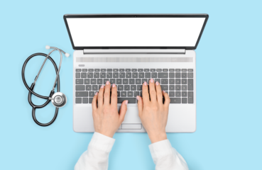 Doctor's hands using laptop with blank monitor on blue background