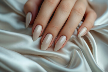 Closeup to woman hands with elegant neutral colors manicure on long almond shaped nails. Female hands with luxury nude shade nail manicure with gel polish on white silk background - obrazy, fototapety, plakaty