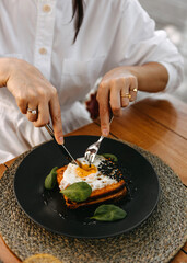 Closeup of a woman enjoying a savory breakfast, with a fried egg on toast, sitting at a wooden table cafe.