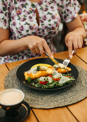 Woman in floral dress enjoying an omelette and salad on a black plate.