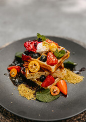 Waffles stacked with fresh berries and sour cream on a dark plate.