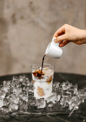 Pouring espresso into a glass of iced milk, surrounded by ice cubes.