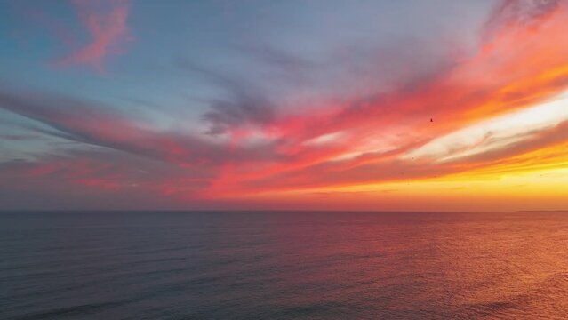 Vibrant colorful sunset clouds over the ocean in Portimao. Flock of seagulls flying away