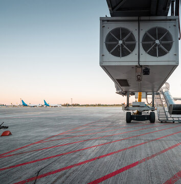 Airport infrastructure - bottom part of jet bridge, that allows passengers to board or disembark directly from terminal. Striped apron in the foreground and few passenger aircraft in the background.