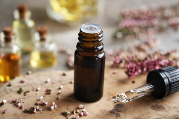 A brown bottle of aromatherapy essential oil with a dropper and pink heather flowers