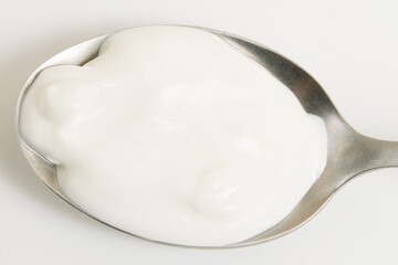 Sour cream or white sauce in a spoon on a white plate close-up