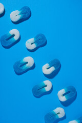 array of two lines of 0 shaped white and blue gummy candies on a blue background, laying in a...
