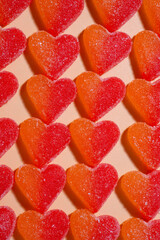 Array of heart-shaped orange and red gummies. laying on a pastel orange surface. Upside view, vertical image