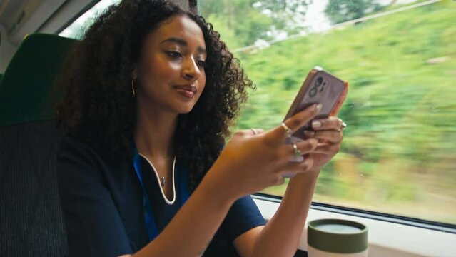 Female doctor or nurse wearing uniform commuting sitting by window on moving train drinking from reusable cup using mobile phone - shot in slow motion