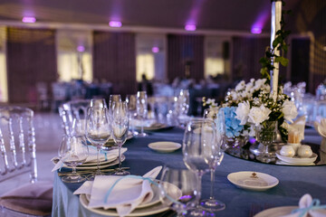 An elegantly set wedding reception table in blue tones with plates, glasses and textile handkerchiefs.