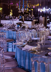 An elegantly set wedding reception table in blue tones with plates, glasses and textile handkerchiefs.