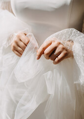 A bride holding her veil, wearing a diamond engagement ring, in sunlight, closeup.