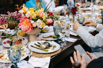 Festive table setting with colorful floral centerpiece, guests dining, fish dish, asparagus, wine, water, and vibrant atmosphere.