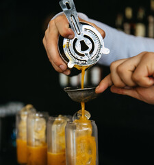 Bartender pouring an orange drink through a strainer into a glass.