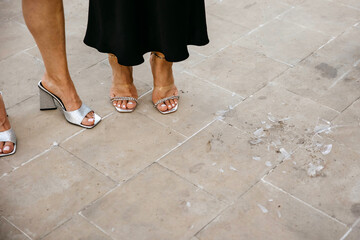 Shattered glass at a party on the floor, next to women's feet in shoes.