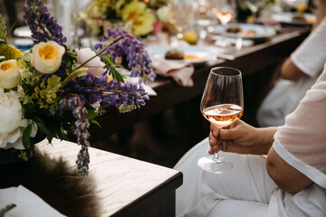 A person holding a glass of rosé wine at an elegantly set table with floral arrangements.