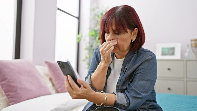 Mature hispanic woman shocked while looking at smartphone in bedroom