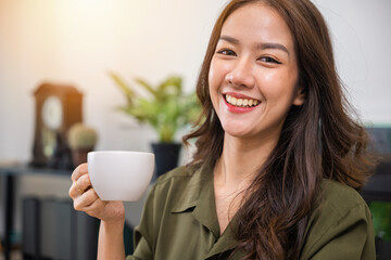 Portrait of Asian young woman holding hot coffee or tea cup in morning while posing, white porcelain mug mock up, Happy beautiful woman relaxing in summer after wakeup at home, lifestyle