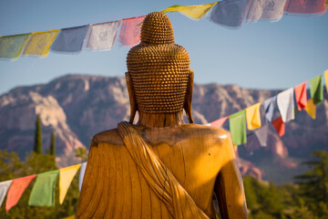 This image shows a rear view of a buddha statue surrounded by prayer flags, overlooking an epic...