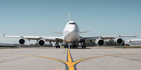 Huge white passenger aircraft taxiing on a sunny day, hot exhaust coming out of the engine and distorts the visibility. Frontal symmetric view of two-storey jumbo jet on a ground.