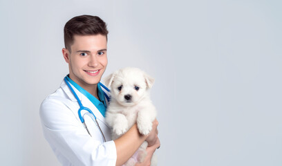 a young veterinarian caucasian  man in a white coat holds a  dag puppy white  in hands on a white background with space for text. Concept: veterinary clinics, love for animals, poster, banner, 