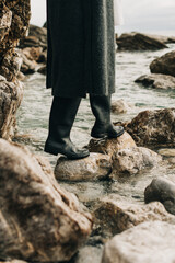 Girl in rubber boots on the rocks by the sea.