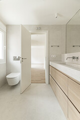 Fototapeta na wymiar A bathroom with sun marble effect tile walls, integrated wall mirror, toilet behind the door