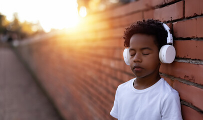 ein Kind Junge mit geschlossenen Augen genießt lehnt an einer Mauer hört Musik durch Kopfhörer, akustischer Genuß aus Klang und Tönen, Teenager allein im Sommer als Hintergrund Vorlage - obrazy, fototapety, plakaty