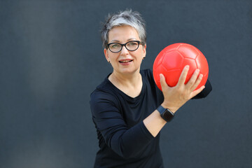 Portrait of a happy and healthy senior woman enjoying recreational activities, kicking a ball in...
