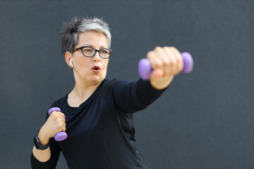 A fit and active senior woman lifting dumbbells in a gym, promoting a healthy and sportive...