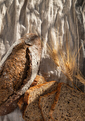 top view: slices and loaf of bread on cloth, bathed in sunlight, surrounded by ears of wheat.