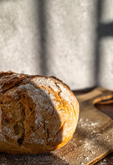 Golden bread loaf, standing out on a wooden board, bathed in warm sunlight. Delicious handcrafted simplicity.