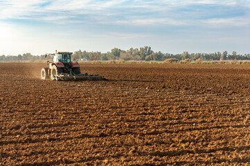 Fototapeta premium Rural Gleams: Backlit Tractor, Plowing a Field at Sunset.