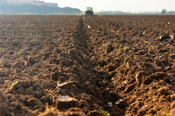 Agricultural Perspective: Furrow at Sunset Leading to the Backlit Tractor.