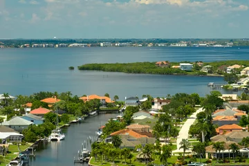 Fotobehang Aerial view of rural private houses in remote suburbs located on sea coast near Florida wildlife wetlands with green vegetation on gulf bay shore. Living close to nature in tropical region concept © bilanol