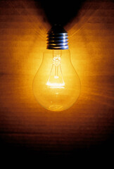 closeup of an old burning light bulb, a carton as background is illuminated, lit with a warm yellow or orange light