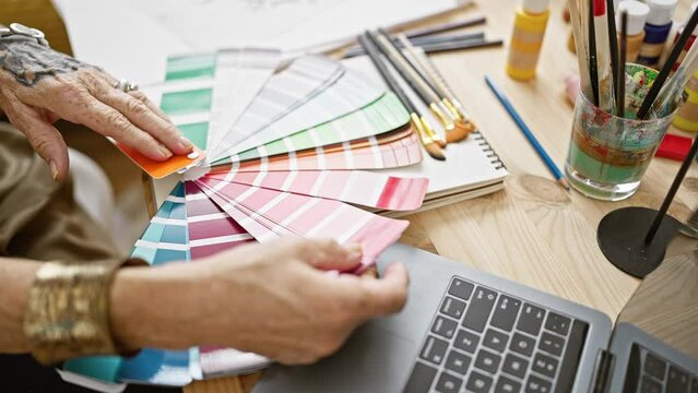 In the heart of an art studio, hands of a senior woman artist are seen choosing a paint color, immersed in her beloved hobby