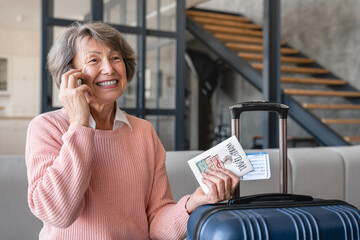 Cheerful old elderly senior happy traveler grandmother woman with airline train tickets calling taxi to airport train station, moving abroad to a new place country for holidays