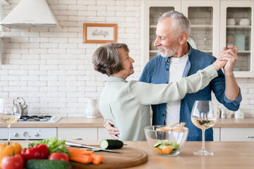 Happy active seniors. Old elderly couple spouses grandparents dancing together while cooking and...