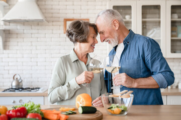 Romantic dinner date concept. Quality time - love language. Caucasian senior couple grandparents celebrating special event anniversary together, cooking and drinking wine at home kitchen